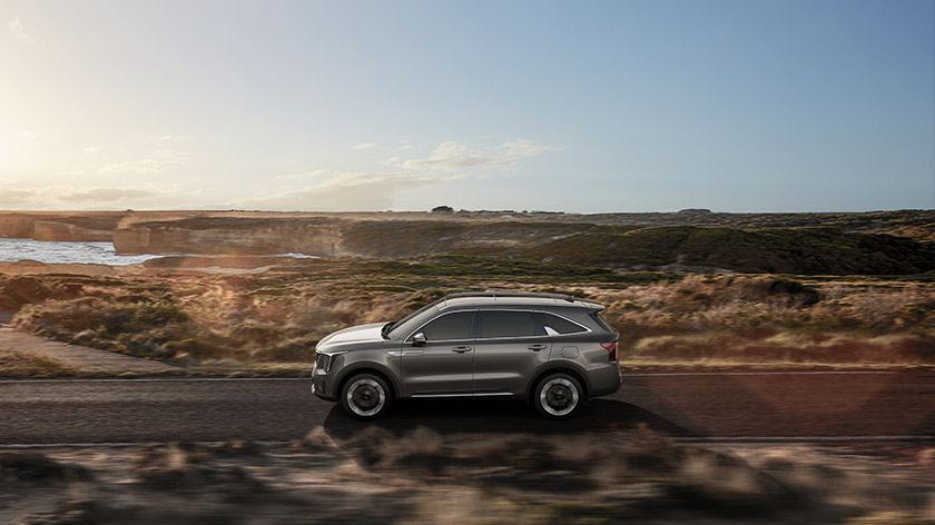 Side view of Kia Sorento driving on a road near the ocean